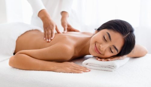 Beautiful Young Indian Woman Enjoying Professional Wellness Massage In Spa Salon, Closeup Shot Of Therapist Lady Massaging Back Of Attractive Client Lying On Table With Closed Eyes